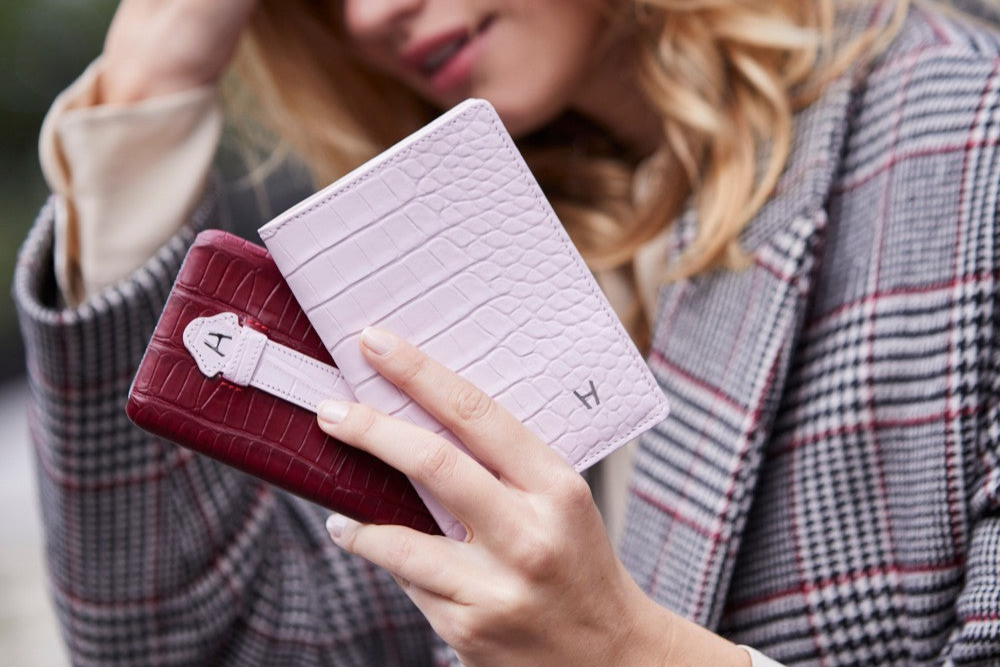 Woman holding two wallets, one red and one pink with a textured pattern, in an outdoor setting.
